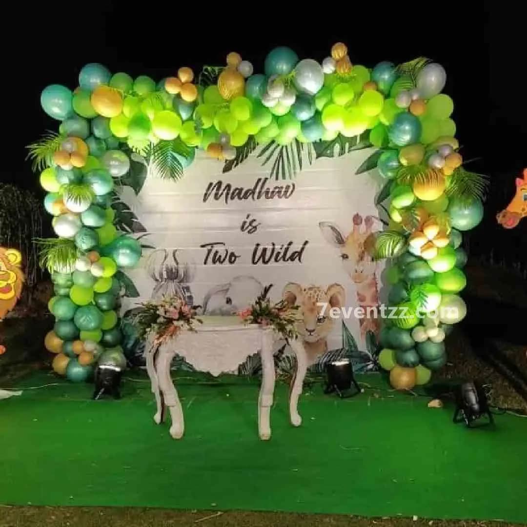 Jungle theme stage setup for kids birthday with large animal backdrop, lush greenery, and balloon arches