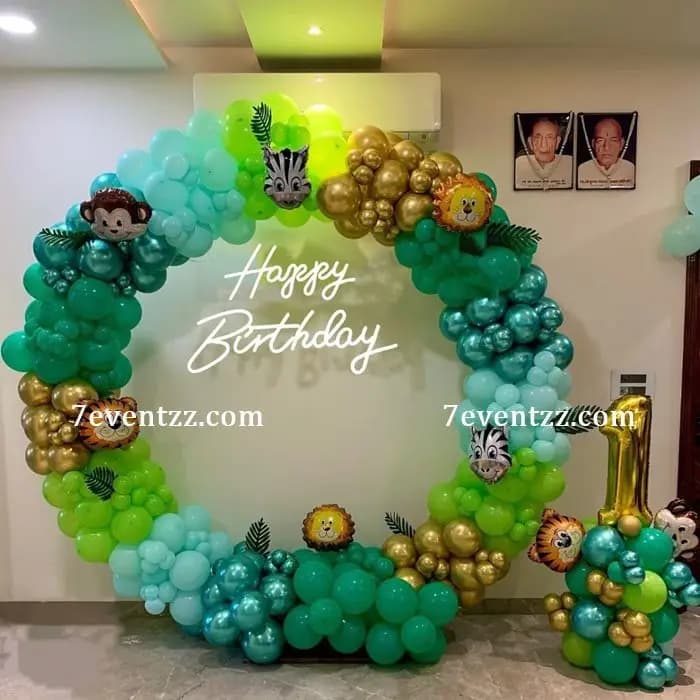 Jungle theme birthday backdrop decoration with tropical leaves, animal props, and green balloon arrangement