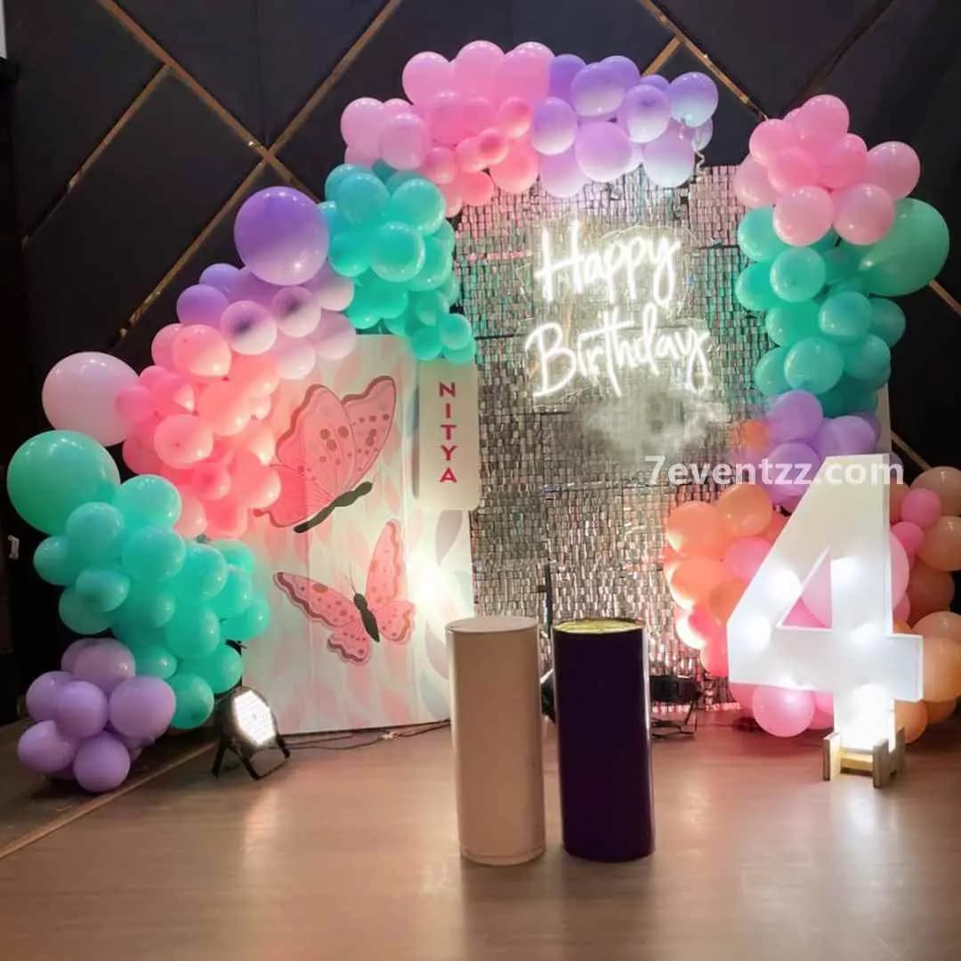 Butterfly themed stage decoration with large butterfly cutouts, drapes, and floral balloon arch