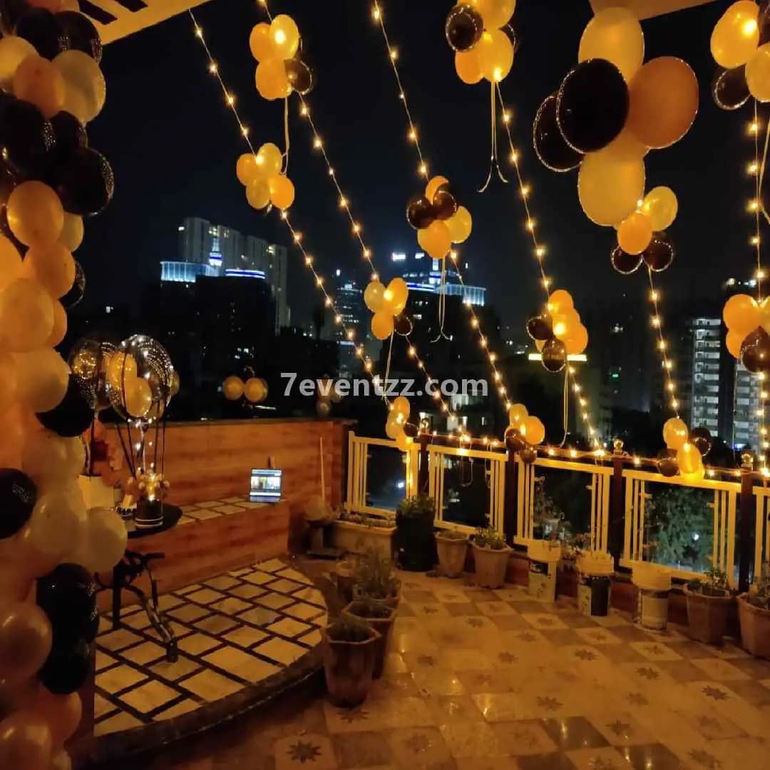 Outdoor terrace night birthday decoration with string lights, balloon arch, and glowing backdrop setup – 7eventzz