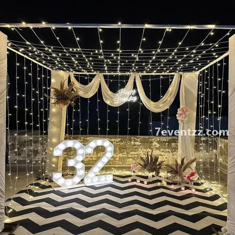 Grand rooftop terrace party setup with balloon pillars, fairy light canopy, and decorated stage backdrop – 7eventzz