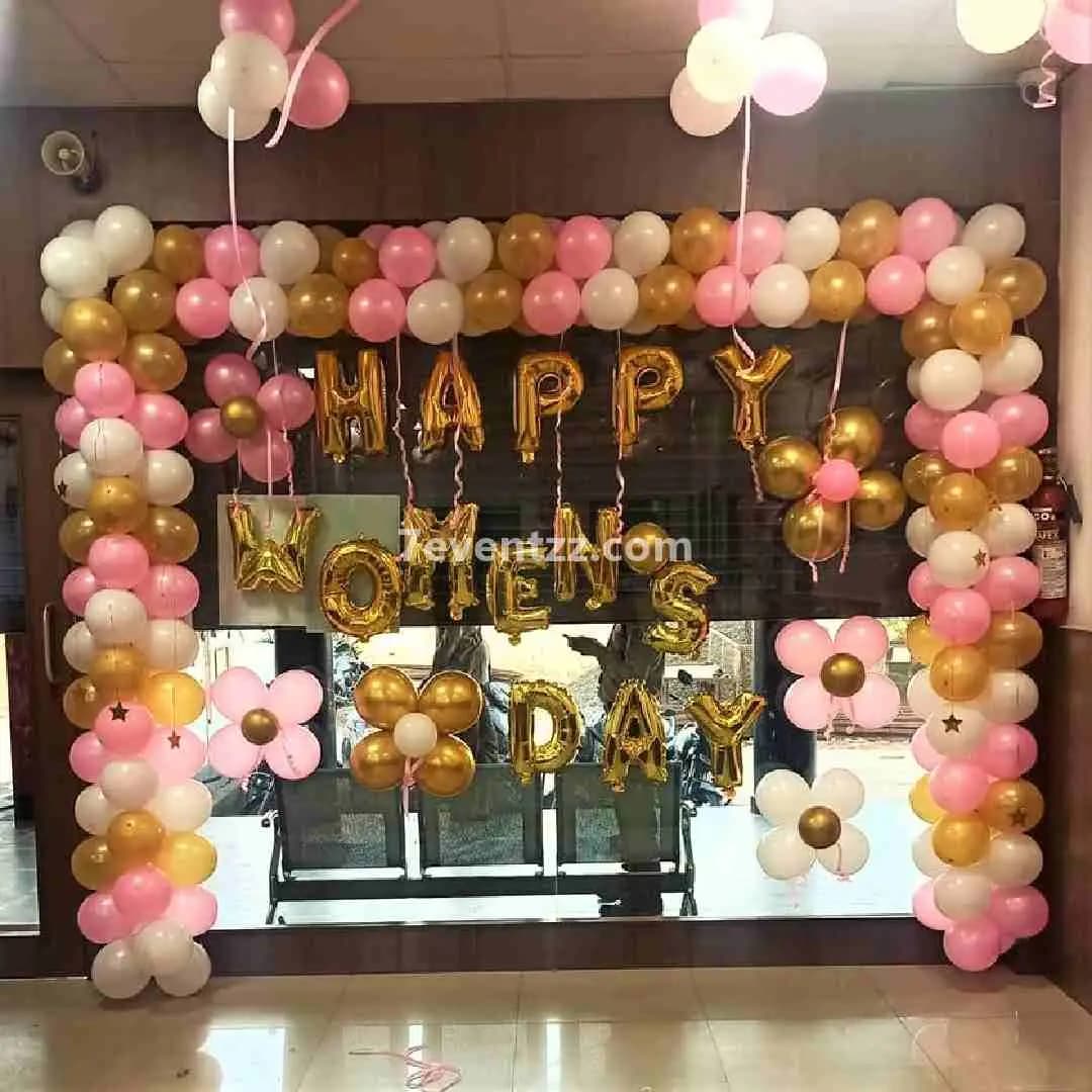 Women's Day office decoration with purple and pink balloons, floral arrangements, and celebratory backdrop