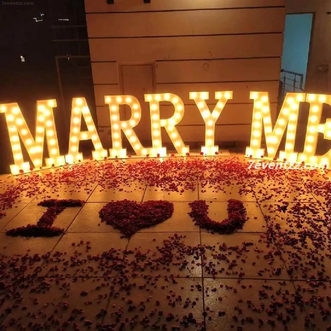 Outdoor proposal setup with floral arch, candles, and string lights at night