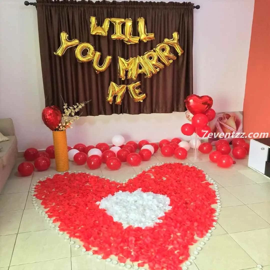 Intimate will you marry me setup with candles, flowers, and balloon lettering